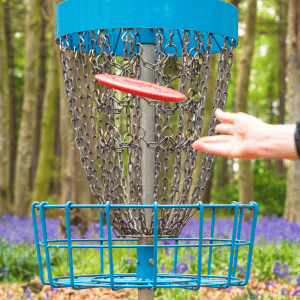A hand throwing a disc into a disc golf cage