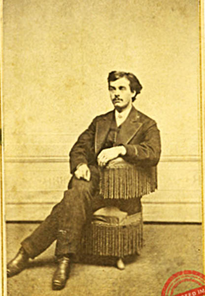Sepia photograph of a young man, Herman D. Squire, seated on a fringed chair, wearing a dark jacket and light shirt.